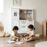 Kids playing in front of the white wooden play kitchen in a bright playroom